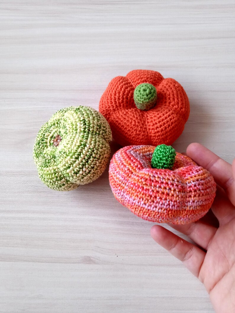 May include: Three crocheted pumpkins in different colors and patterns. One is green and white, one is orange and white, and one is orange and pink.