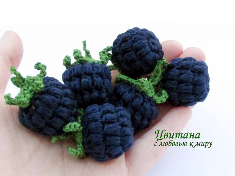K&ouml;nnte beinhalten: Eine Hand h&auml;lt eine Gruppe geh&auml;kelter Brombeeren. Die Brombeeren sind aus dunkelblauem Garn gefertigt und haben gr&uuml;ne geh&auml;kelte Bl&auml;tter. Der Text "Цвитана с любовью к миру" ist in der rechten unteren Ecke des Bildes sichtbar.