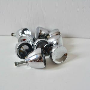 May include: A collection of small, rounded cabinet knobs with a polished chrome finish. Each knob features a smooth, reflective surface and a short metal screw extending from the back for installation. The knobs are grouped together in a cluster.