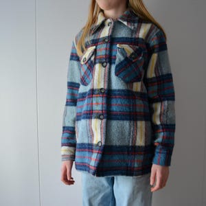 May include: A vintage plaid shirt in shades of blue, red, and yellow. The shirt features a button-down front, two chest pockets, and a classic collar. The fabric has a textured appearance.