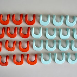 May include: Rows of orange and light blue U-shaped objects. The objects are evenly spaced and arranged in parallel rows. The color palette is simple, with the orange and light blue contrasting against a neutral background. The objects appear to be made of a smooth, solid material.