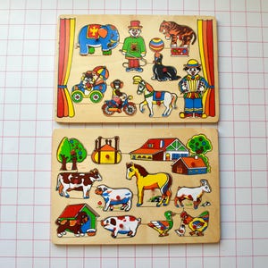 May include: Two wooden jigsaw puzzles with bright illustrations. One shows circus animals such as an elephant, tiger, and seal. The other depicts farm animals, including a cow, horse, and duck. Each puzzle piece fits into a corresponding slot on the wooden base.