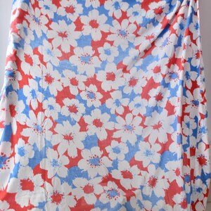May include: A piece of fabric featuring a repeating floral pattern with white flowers, red petals, and blue accents. The design covers the entire surface of the textile, creating a dense, layered arrangement of blossoms across the white background.