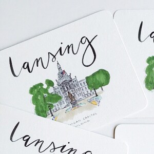 May include: Square postcards with watercolor illustrations of the Michigan State Capitol Building in Lansing. The word "Lansing" is written in cursive above the image. The back of one postcard is visible, with lines for an address and a stamp box.