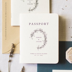 May include: Cream-colored passport with the word "PASSPORT" in dark purple. The passport features a floral wreath design and the names "SARAH & CALEB" with the location and date "TURKS & CAICOS ISLANDS 05/15/2021".
