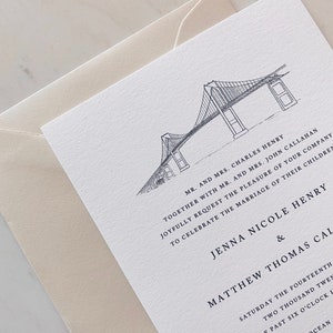 May include: Wedding invitation with a detailed black and white illustration of a suspension bridge. The invitation includes the names of the couple, the date, and time of the ceremony, and is accompanied by a cream-colored envelope.