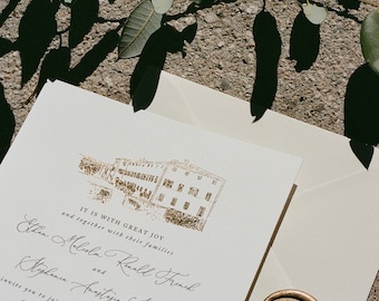May include: Wedding invitation with gold foil details, including a building illustration and elegant script. The invitation is on cream-colored paper, sealed with a gold wax stamp featuring a leaf design. Green leaves and shadows are in the background.