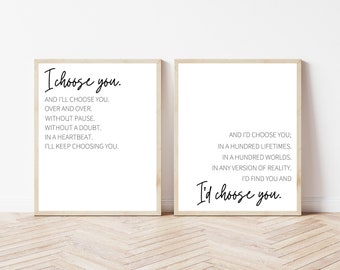 May include: Two framed prints with romantic quotes in black script on a white background. The first print reads "I choose you" with accompanying text. The second print says "I'd choose you" with additional text. Both are in light wood frames.