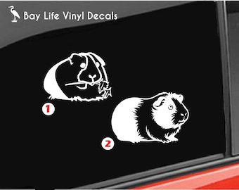 May include: A white vinyl decal featuring two guinea pig designs on a black background. The first design shows a guinea pig eating a leaf, labelled with the number 1. The second design shows a standing guinea pig, labelled with the number 2. The text Bay Life Vinyl Decals is visible in the top left corner.