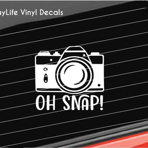 May include: White vinyl decal of a camera with the text "OH SNAP!" on a black background.