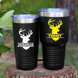 May include: Two black stainless steel tumblers with a white deer head design and a name on each. The tumbler on the left says "Joshua" and the tumbler on the right says "Timmy".