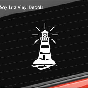 May include: White vinyl decal of a lighthouse with a beam of light shining from the top. The lighthouse is on a small island with waves around it.