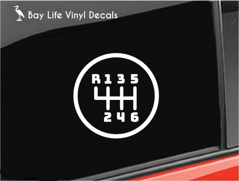 May include: White vinyl decal of a car's manual transmission gear shift pattern, with R, 1, 2, 3, 4, 5, and 6 clearly labeled. The decal is set against a black background, with the text "Bay Life Vinyl Decals" in the upper left corner.