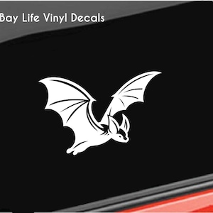 May include: White vinyl decal of a bat with wings spread, flying in a black background. The decal is for a car window or other smooth surface.