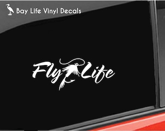 May include: A white vinyl decal applied to a black car window featuring the text Fly Life in a cursive script font. The letter y in Fly is replaced by a graphic illustration of a fishing fly lure with a hook and feathered tail.