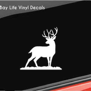 May include: White vinyl decal of a deer with large antlers, standing on a patch of grass. The decal is applied to a black surface, with the text "Bay Life Vinyl Decals" in the upper left corner.