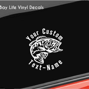 May include: White vinyl decal featuring a detailed illustration of a bass fish with an open mouth. The text "Your Custom Text-Name" is arched around the fish. The decal is set against a black background, with the words "Bay Life Vinyl Decals" in the upper left corner.