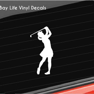 May include: White silhouette of a person playing golf on a black background. The person is holding a golf club and is in the middle of their swing. The silhouette is a vinyl decal.
