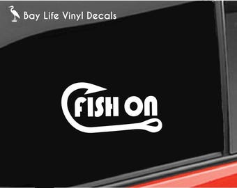 May include: A white vinyl decal applied to a black car window. The design features a large fishing hook shape that curves around the text "FISH ON" in a bold, sans-serif font. The top left corner displays the text "Bay Life Vinyl Decals".