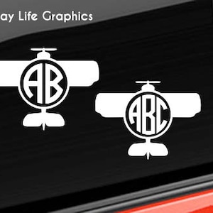 May include: Two white vinyl decals of a plane with a circle monogram in the center. The top decal has the monogram "AB" and the bottom decal has the monogram "ABC".