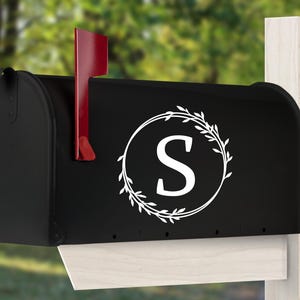 May include: Black mailbox with a white wreath and the letter "S" in the center. The mailbox has a red flag.