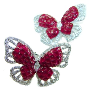 May include: Two butterfly-shaped brooches. The wings are made of small, square-cut, deep red gemstones. The edges of the wings are outlined with small, clear gemstones. A larger, clear gemstone is in the center of each butterfly.