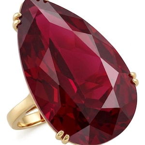 May include: A gold ring featuring a large, pear-shaped, deep red faceted gemstone. The stone is secured by four small gold prongs at the top, bottom, and sides, set against a polished gold band that curves to support the prominent, vibrant red center.
