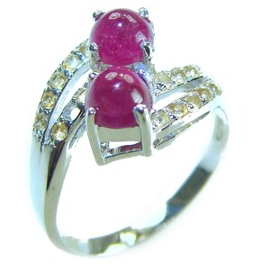 May include: A silver ring featuring two oval, deep red gemstones. The ring is accented with smaller, yellow-toned stones along the band. The gemstones are set in a prong setting, and the ring has a polished finish.