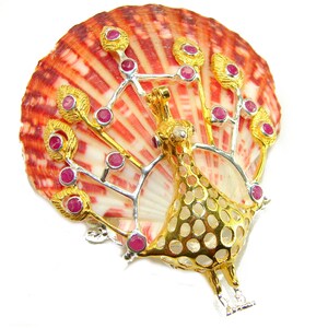May include: A gold and silver peacock brooch with ruby accents, set against a red and white seashell. The peacock's body features a detailed openwork design. The brooch is a unique piece of jewelry.