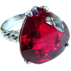 May include: A silver ring with a large, faceted, pear-shaped, deep red gemstone. The ring's band has a twisted rope design, and the gemstone is held in place by small silver prongs.