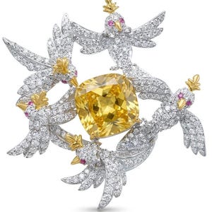 May include: A brooch featuring four silver-toned birds encrusted with clear stones, each with a gold-toned crest and beak and small pink eyes. The birds are arranged in a circular formation around a large, central, cushion-cut yellow stone.