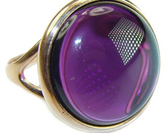 May include: A purple glass ring with a gold setting. The ring has a unique design with a pattern of small dots on the glass.