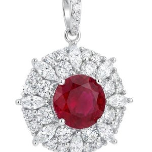 May include: A circular pendant necklace featuring a large, round, deep red ruby at the center. The ruby is surrounded by a halo of alternating marquise-cut and round-cut clear white diamonds set in silver-toned metal, with a diamond-encrusted bail.