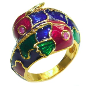 Peut inclure: Une bague en or avec un motif en émail coloré. Le motif représente un poisson stylisé avec de l'émail bleu, vert, rouge et rose. La bague est sertie de petites pierres précieuses roses.