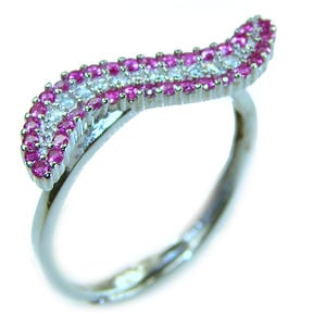 May include: A silver ring with a wave-like design. The wave is encrusted with alternating rows of small, round, pink and white gemstones. The ring is set against a white background, highlighting the sparkle of the stones.