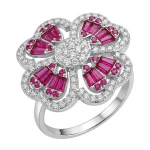 May include: A silver-toned ring featuring a large flower-shaped centrepiece. The petals are adorned with baguette-cut red stones and small round red stones, while the centre and the outer edges are encrusted with numerous small clear white stones.