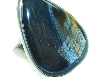 May include: A statement ring with a large, teardrop-shaped blue tiger's eye stone. The stone, with gold and brown streaks, is set in a silver-coloured metal band. A striking piece of jewellery.