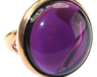 May include: A ring with a large, oval-shaped, purple gemstone set in a gold-toned metal band.