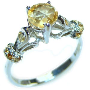 May include: A silver ring with a large, round, yellow topaz gemstone. The ring has a delicate, intricate design with smaller topaz gemstones on the band.