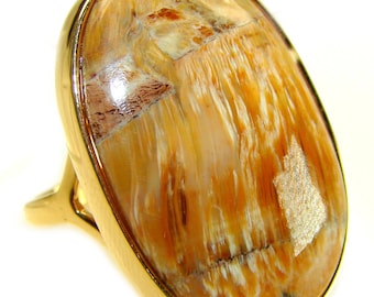 May include: A gold ring with an oval stone. The stone has a distinctive pattern of light brown, beige, and reddish-brown colours. The stone is set in a polished gold band, creating a striking contrast.