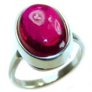 May include: A silver ring with a large, oval-cut, deep pink gemstone. The gemstone has a polished, glossy surface with lighter, swirling inclusions. The ring's band is a simple, polished silver design, highlighting the prominent gemstone.