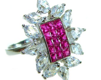 Könnte beinhalten: Ein silberner Ring mit einem rechteckigen, leuchtend rosa Edelstein in der Mitte, umgeben von klaren, tropfenförmigen Steinen. Das Design des Rings erinnert an eine Blume, wobei der rosa Stein im Mittelpunkt steht.