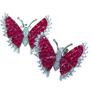 May include: A pair of butterfly-shaped earrings. The wings are composed of small, square, deep red stones, outlined with a border of small, clear, round stones. The butterfly bodies are silver-colored with clear stones.