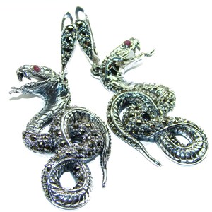 May include: A pair of silver snake earrings. Each earring features a detailed snake design with marcasite accents and a red gemstone eye. The snakes are coiled and have a hook closure.