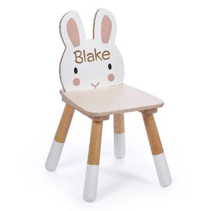 May include: A white wooden children's chair shaped like a bunny with pink ears. The chair has a natural wood seat and legs with white painted accents. The chair is personalised with the name "Blake" on the front.
