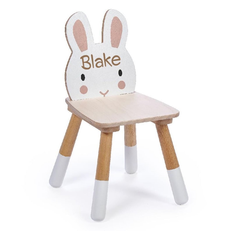 May include: A white wooden children's chair shaped like a bunny with pink ears. The chair has a natural wood seat and legs with white painted accents. The chair is personalised with the name "Blake" on the front.
