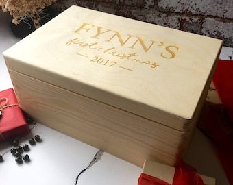 Puede incluir: Una caja de madera para recuerdos con la inscripción "Fynn's First Christmas - 2017" en la tapa. La caja está hecha de madera natural y tiene un color marrón claro.