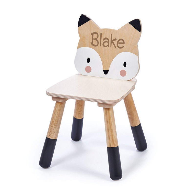 May include: A wooden children's chair with a fox face on the back. The chair is painted brown with black accents and the fox face has a white nose and pink cheeks. The name "Blake" is written on the fox's forehead.