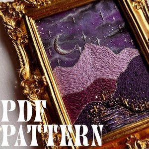 Op de afbeelding: Geborduurd kunstwerk in een gouden, sierlijke lijst. De afbeelding toont een nachthemel met een halve maan en sterren boven paarse en kastanjebruine bergen. De tekst "PDF PATTERN" is over de afbeelding geplaatst.
