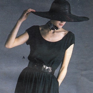 May include: A woman wearing a black dress with a wide black hat and a black belt with a silver buckle. The dress has a flowing skirt.